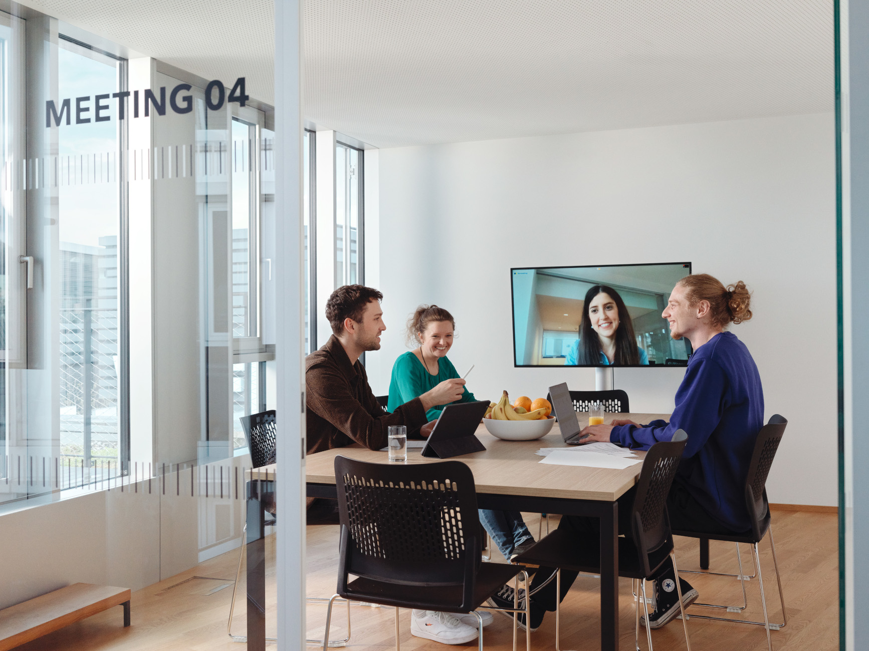 Menschen in einem Büro, welche mit einer weiteren Person per Videokonferenz kommunizieren.